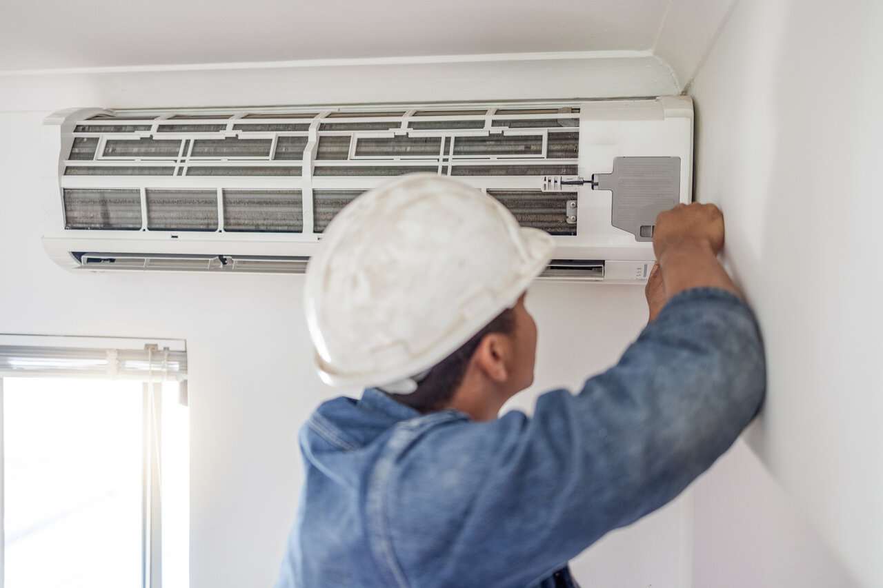 A man in a hard hat repairs an air conditioner.