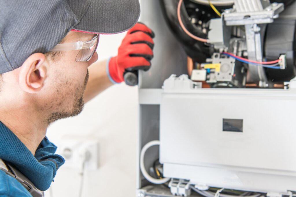 Heater Repair in Truckee, CA 1 A man wearing a hard hat and safety glasses repairs a gas furnace.