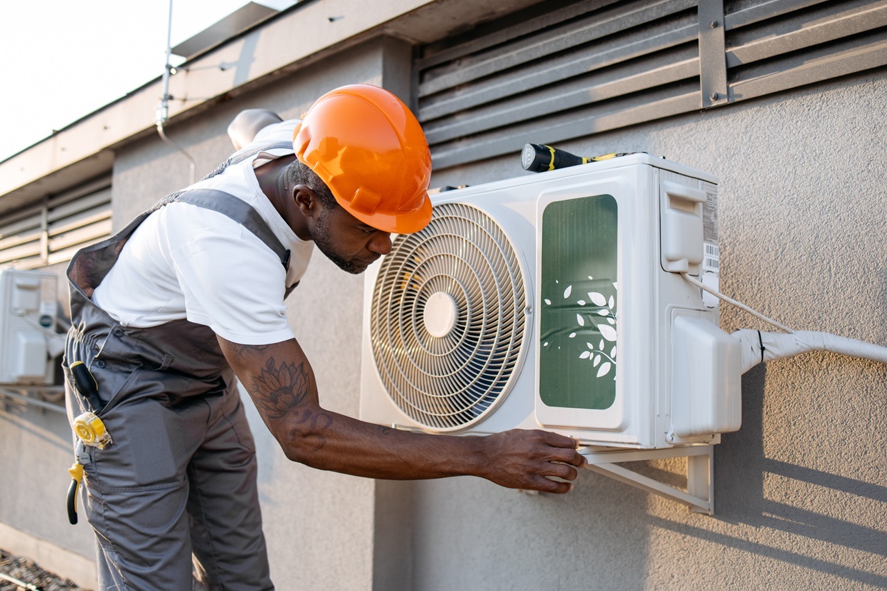 A man in overalls and a hard hat repairs an air conditioner.