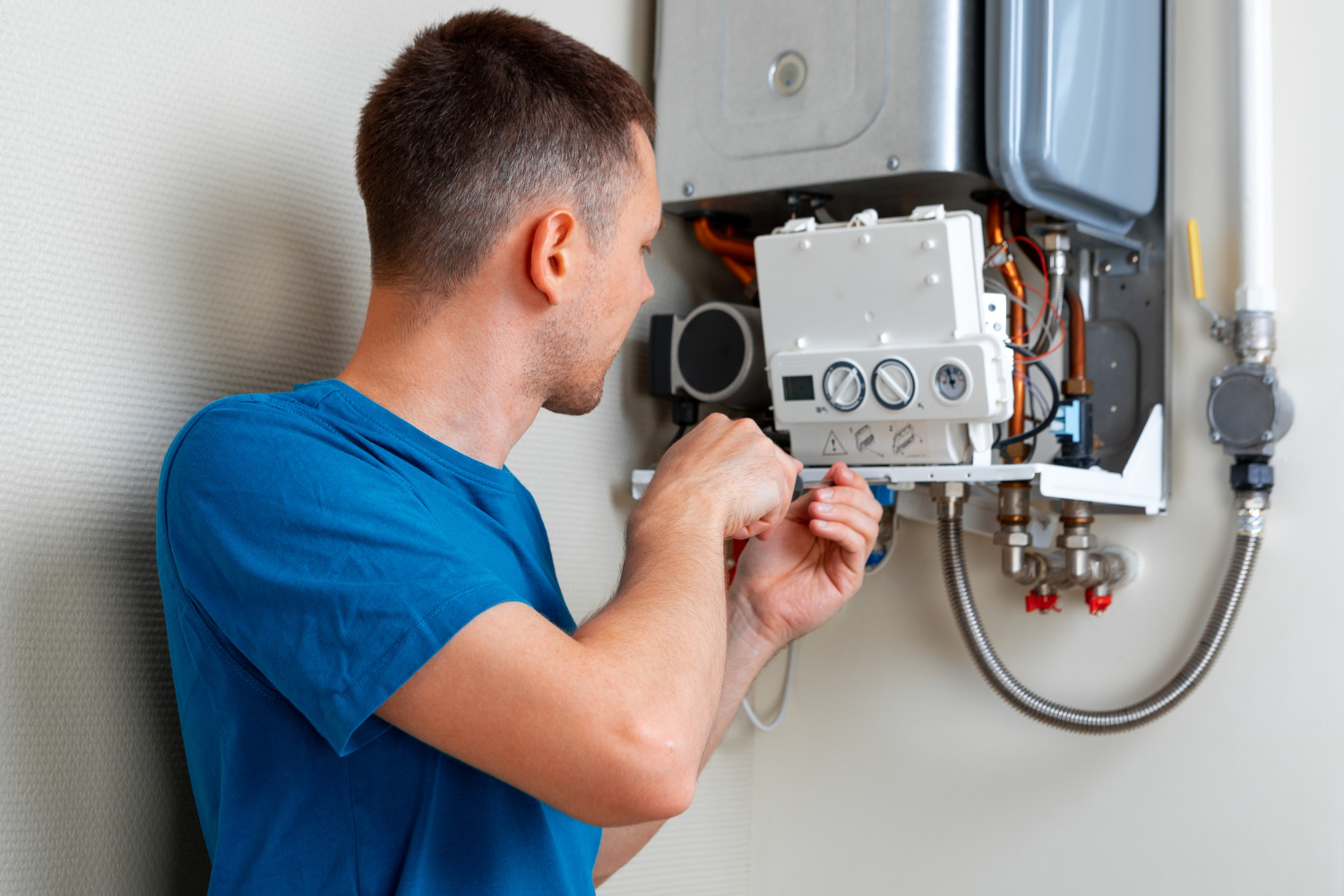 A man repairs a gas boiler in a utility room, focused on the equipment.